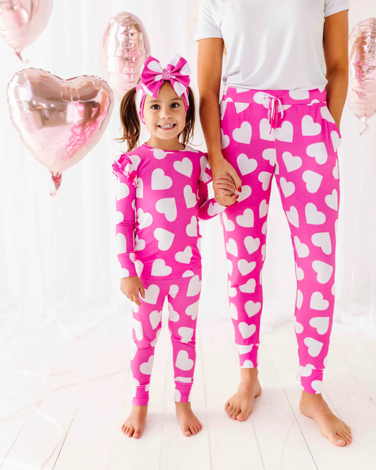 Child and adult wearing matching pink pajamas with white hearts